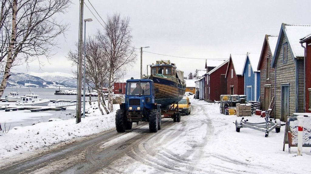 Ein Traktor zieht ein Boot auf dem Anhänger durch einen verschneiten Hafenort